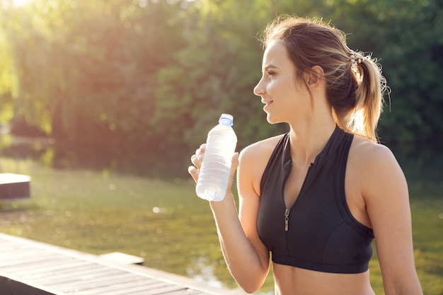 Young beautiful woman drinking water during morning jogging in the park