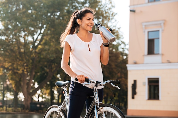 Young beautiful woman drinking water from the bottle and sitting on the bike