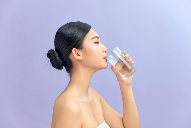 Молодая красивая женщина пьет воду из стекла на белом фоне