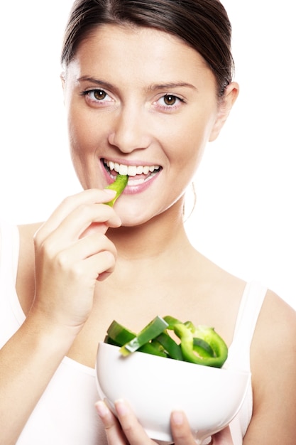 Una giovane bella donna che mangia pepe verde su sfondo bianco