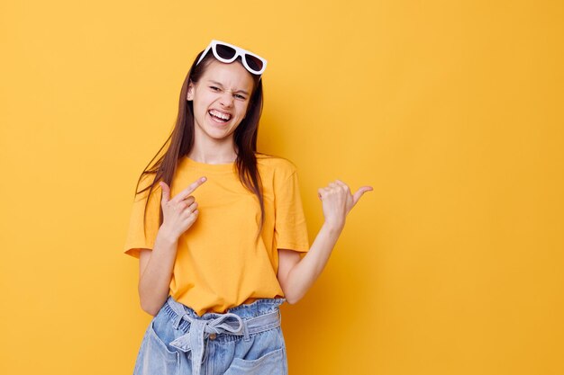 黄色のTシャツデニムショートパンツ黄色の背景で若い美しい女性のファッション