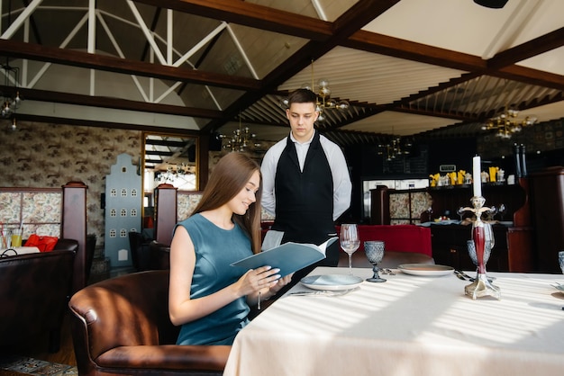 A young beautiful woman in a fine restaurant looks at the menu\
and makes an order to a young waiter in a stylish apron. customer\
service.