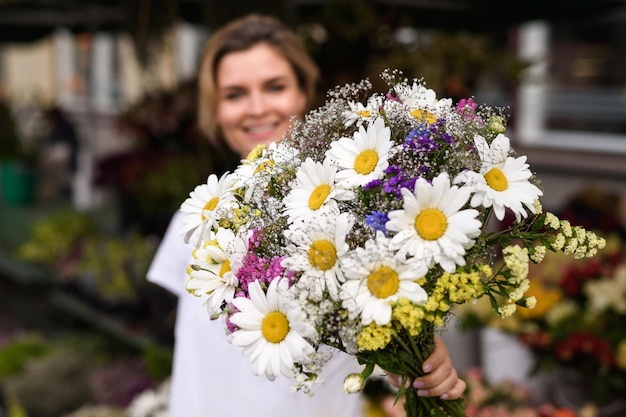 彼女の小さな花屋で野花の花束を持つ若くて美しい女性の花屋