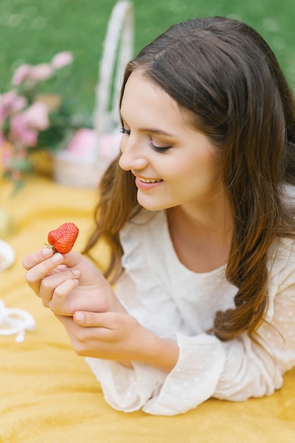 若い美しい女性は夏のピクニックで熟した新鮮なイチゴを優しく泣きます