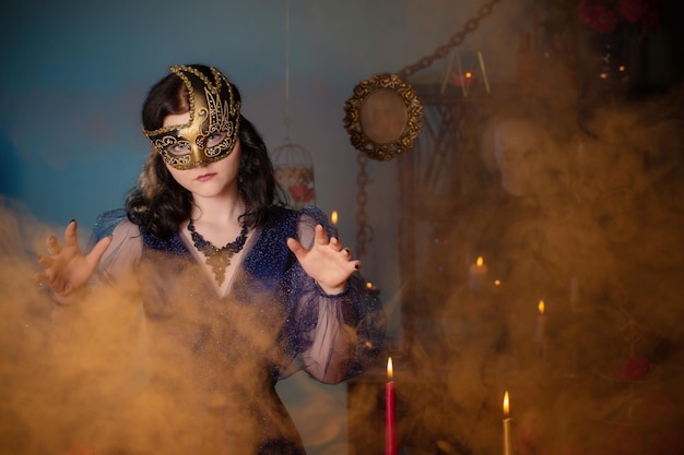 Young beautiful woman in golden mask and blue vintage dress in dark room