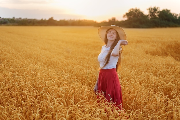 Giovane bella donna con cappello in piedi tra gli steli di grano maturo. la tranquillità