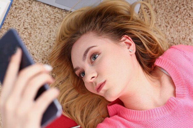 Young beautiful woman have a rest lie on the floor hold smartphone in arms