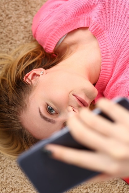 Young beautiful woman have a rest lie on the floor hold smartphone in arms