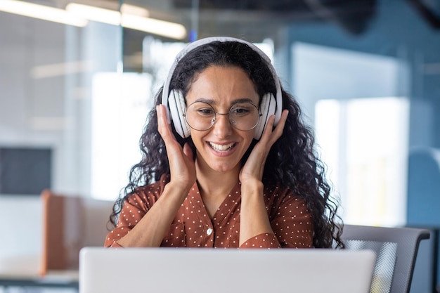 young beautiful woman in headphones working with laptop inside office at workplace joyful and satisfied business woman watching online webinar educational video course learning remotely