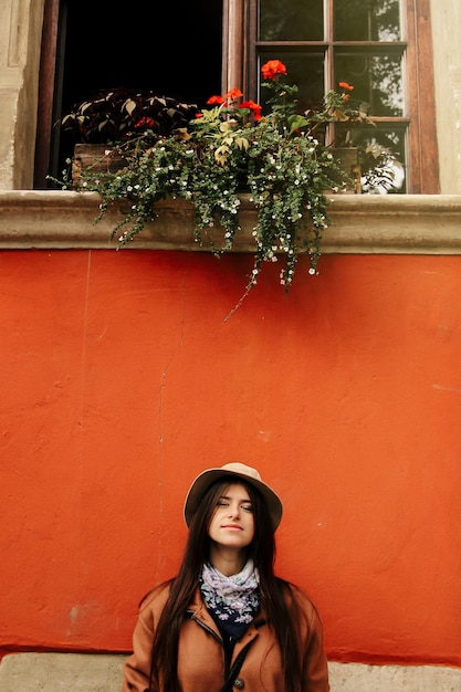 Young beautiful woman hipster standing at red wall and window in the street of an old European town