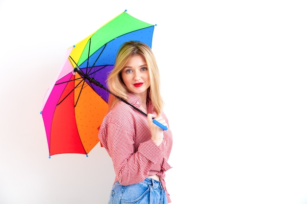 Young beautiful woman holding colored umbrella on white wall