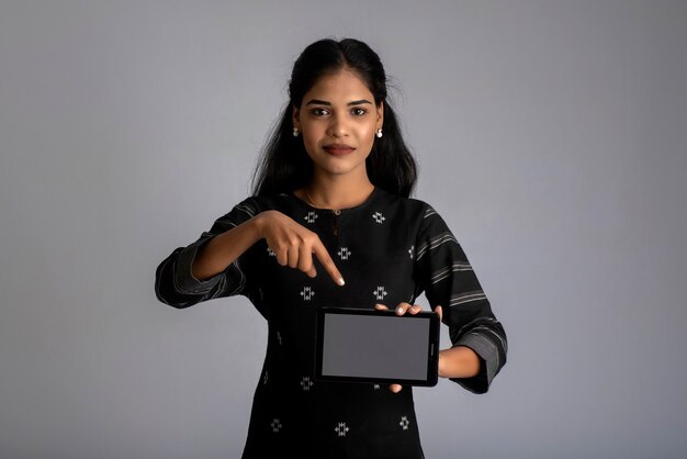 Young beautiful woman holding and showing blank screen of smartphone or mobile or tablet phone on a gray.