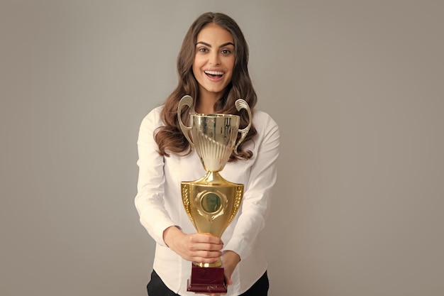 Young beautiful woman holding trophy over grey background Woman holding a trophy