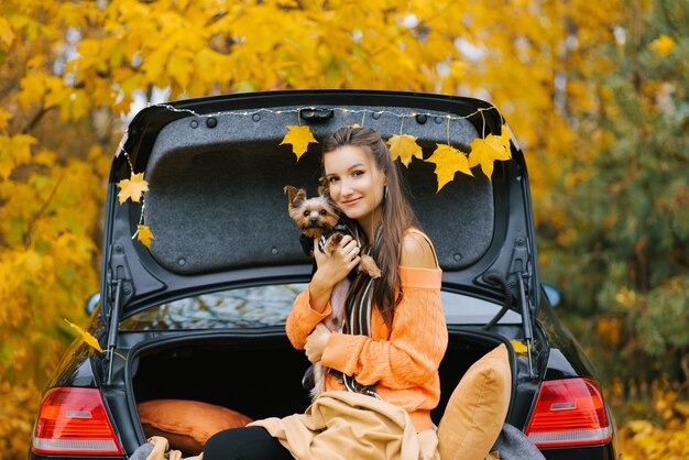 Una giovane bella donna tiene il suo amato animale domestico all'aria aperta contro un bosco in autunno. concetto di viaggio