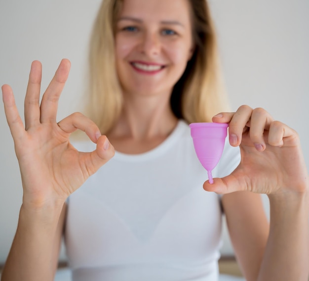 Young beautiful woman at home holding a menstrual cup in her hands