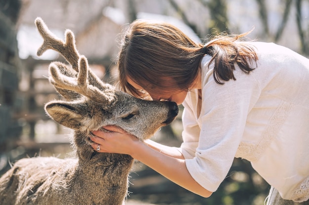 Young beautiful woman hugging animal ROE deer in the sunshine, protecting an animal