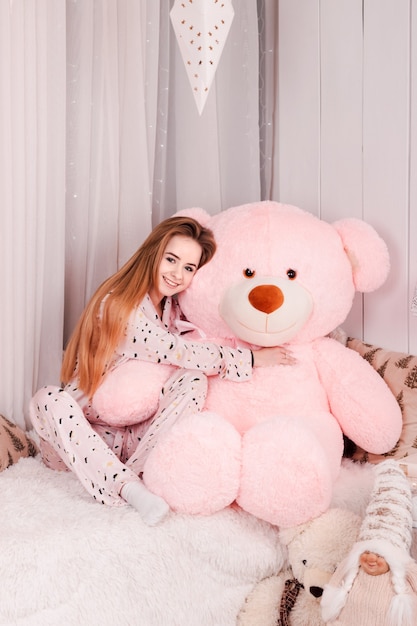 Young beautiful woman hugs pink teddy bear on bed