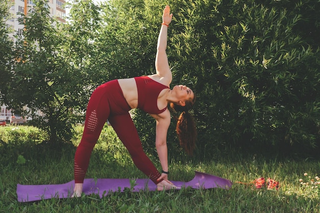 Фото Красивая молодая женщина в красных леггинсах и топ практикует йогу в городском парке