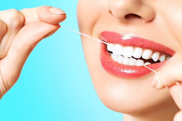 Young beautiful woman is engaged in cleaning teeth. Beautiful smile healthy white teeth. A girl holds a dental floss. The concept of oral hygiene.