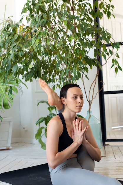 Young beautiful woman is engaged in stretching in a room with plants.