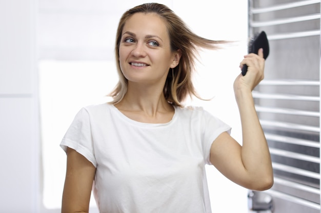 Photo young beautiful woman is looking at her reflection in bathroom and combing her hair