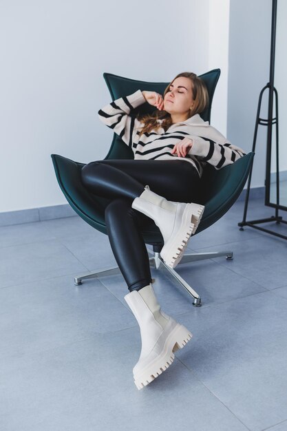 Photo a young beautiful woman is sitting in a chair wearing white leather boots from a new collection of shoes for spring