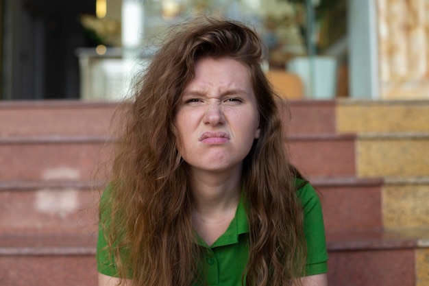 Young beautiful woman is sitting on steps near hotel or new house home and upset