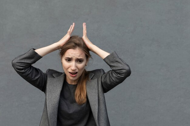 Young beautiful woman is standing in a gray business suit. The business woman is in a panic, she has horror on her face.