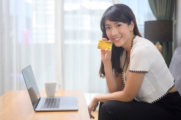 Una giovane bella donna sta usando la carta di credito per lo shopping online sul sito internet a casa, concetto di e-commerce