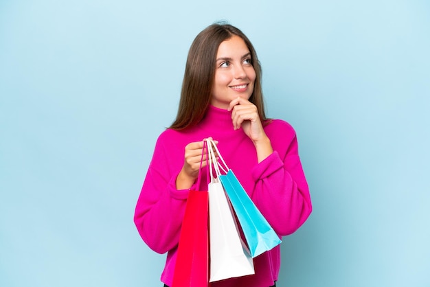 young beautiful woman isolated on blue background holding shopping bags and thinking