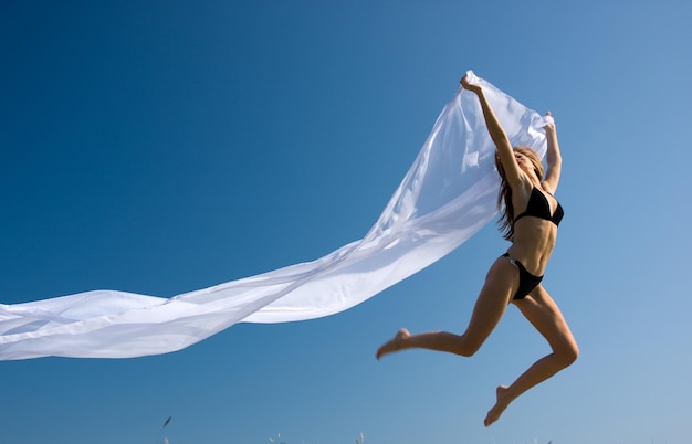 Young beautiful woman jumping with white material