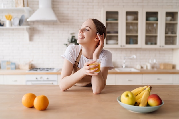 Young beautiful woman in the kitchen in an apron, fruits and orange juice