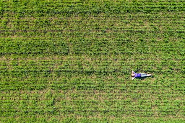 若い美しい女性は晴れた日に緑の野原に横たわってリラックスします。航空写真。