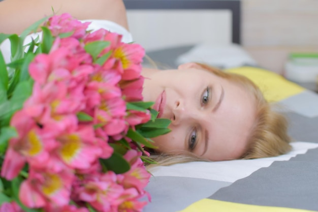 Young beautiful woman lies on bed with a bouquet of fresh flowers