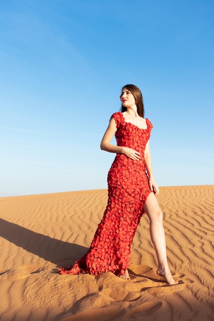 Young beautiful woman in long red dress with red rose petals among the desert Desert rose conception