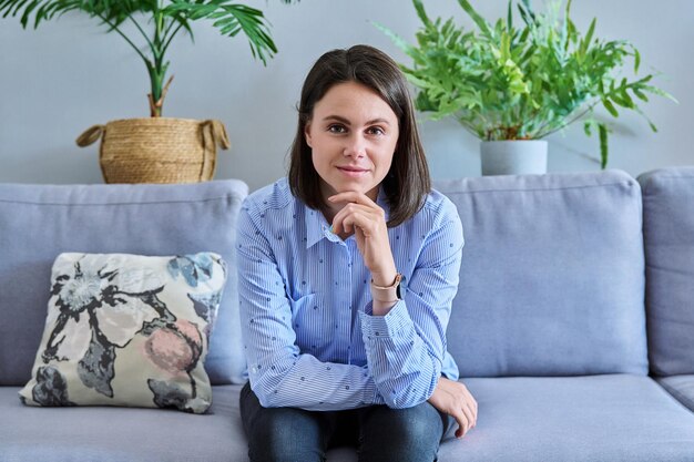 Foto giovane bellissima donna che guarda la telecamera mentre è seduta sul divano a casa ritratto di un sorridente uomo d'affari insegnante donna lavoratore studente freelance vlogger bellezza lavoro lavoro persone 20 anni concetto