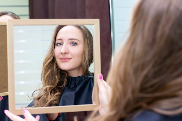 Young beautiful woman looks in the mirror in a beauty salon. Makeup and hairstyle