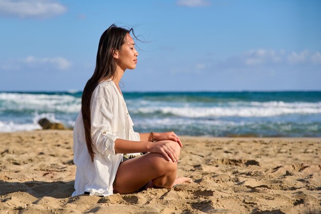 Young beautiful woman in lotus position meditating on the beach