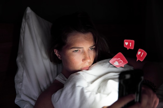 Young beautiful woman lying in bed with smartphone receiving likes and comments on social media in i...