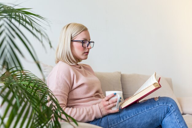 ソファーで横になっていると、家で本を読んで若い美しい女性。素晴らしい本。晴れた朝に本を読んで美しい若い女性。