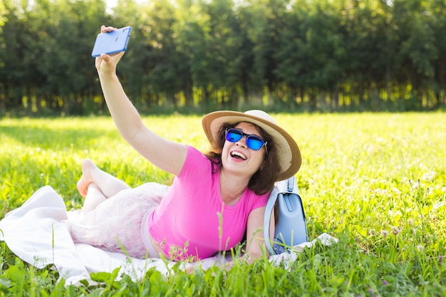 Young beautiful woman make selfie photo on smartphone at a picnic in the summer.