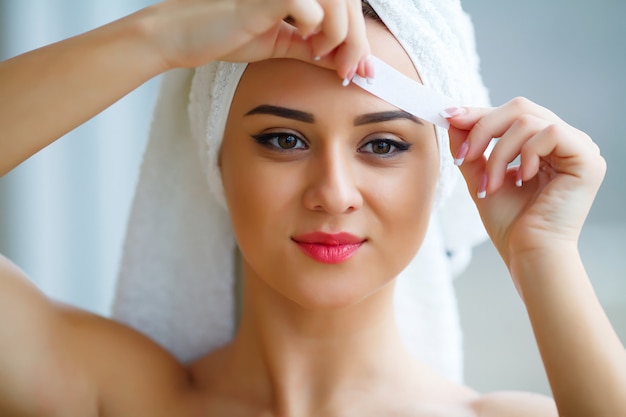 Young beautiful woman makes wax eyelids in her bathroom.