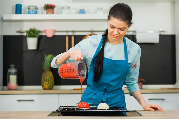 Young beautiful woman making mousse pastry, gelatin dessert in process, red mirror icing