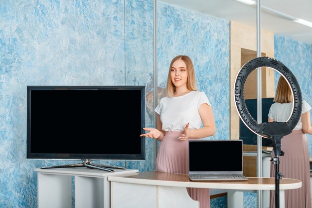 Giovane bella donna che fa presentazione con monitor e laptop modello di visualizzazione vuoto modello di schermo vuoto per tv e laptop presentatore di streaming online con formazione online di insegnante lampada ad anello