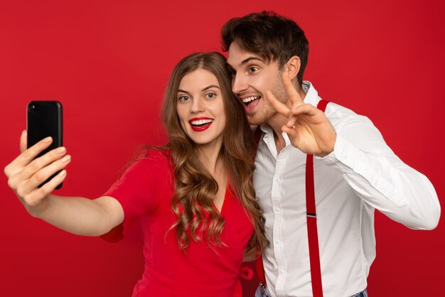 Young beautiful woman and man embrace in elegant outfits taking selfie