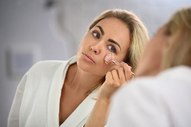 Young beautiful woman massages her face with a roller massager under the eyes, to smooth the skin around the eyes