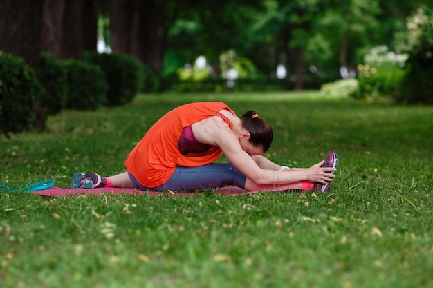 Young beautiful woman meditates on a summer day in the park Idea and concept of calm in a busy city and a healthy lifestyle stretching and preparing for a run in the park