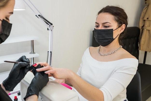 Young beautiful woman in a nail salon paints her nails with red polish Focus on the girl