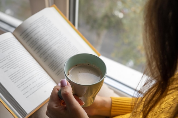 Foto giovane bella donna vicino alla finestra maglione lavorato a maglia giallo leggere il libro