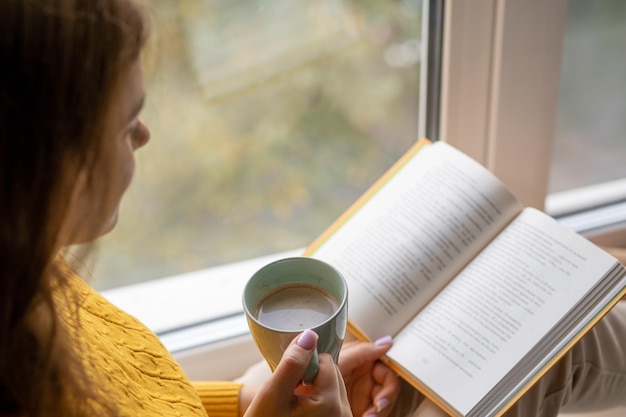 Foto giovane bella donna vicino alla finestra maglione lavorato a maglia giallo leggere il libro